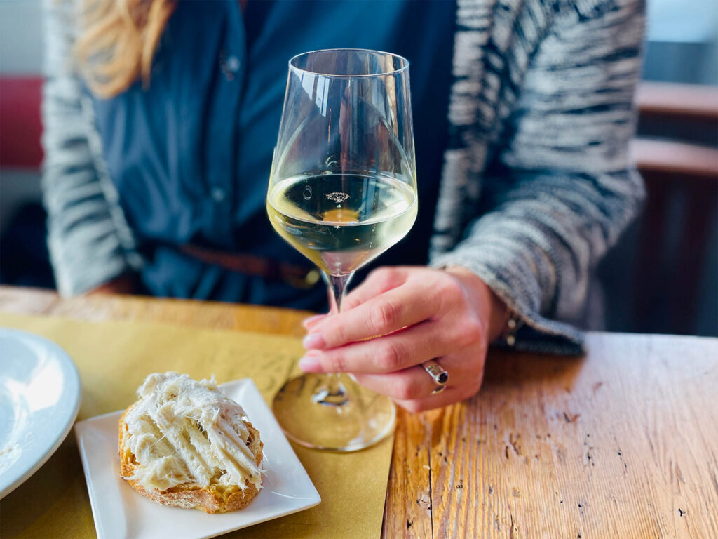 SweedItaly food and drinks image showing a hand holding a wine glass and cicchetti on a table.