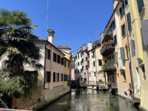Historic canal in Treviso, Italy, with colorful Venetian-style buildings and crystal-clear water on a summer day.