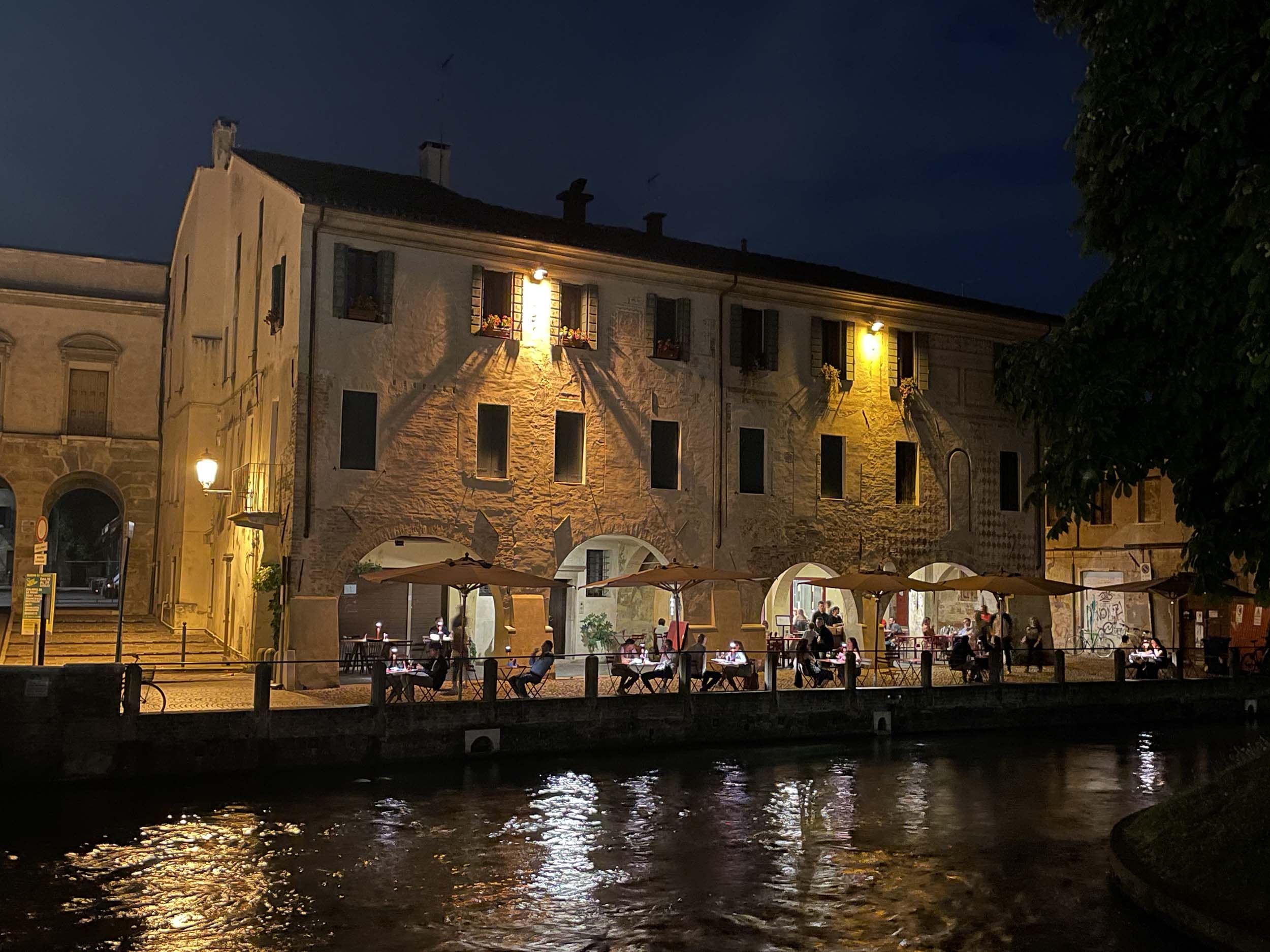 Historic buildings and outdoor restaurants along the canal in Treviso's Pescheria district at night, Italy.
